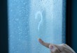 Female hand draws a question mark on a foggy window during the r