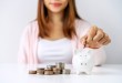 Stack of coins with young woman putting coin into the piggy bank, Saving money for future investment concept
