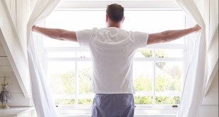 Rear View Of Man Opening Curtains And Looking Out Of Window